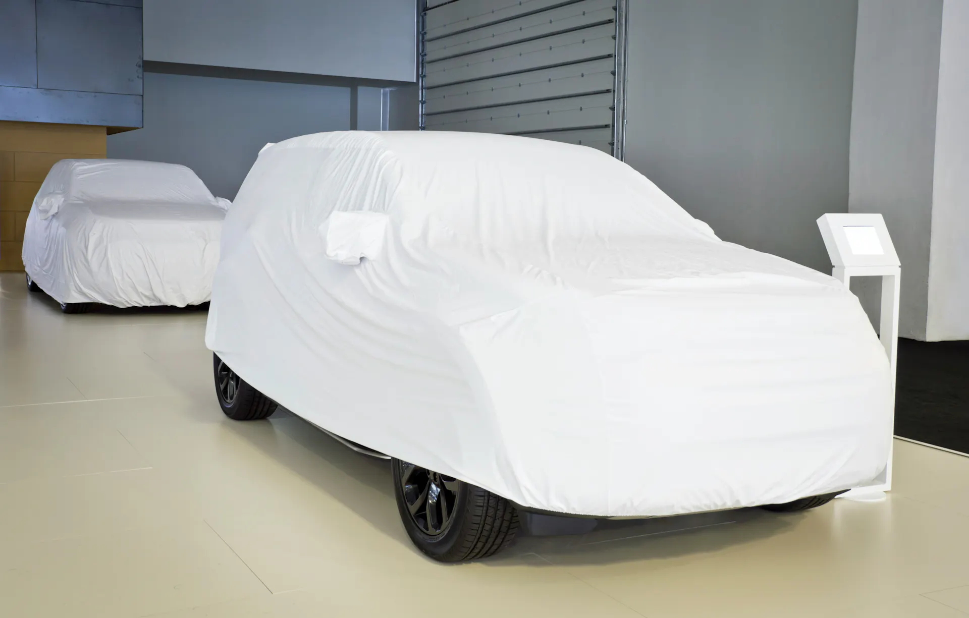 Two cars covered in sheets inside of a storage unit.