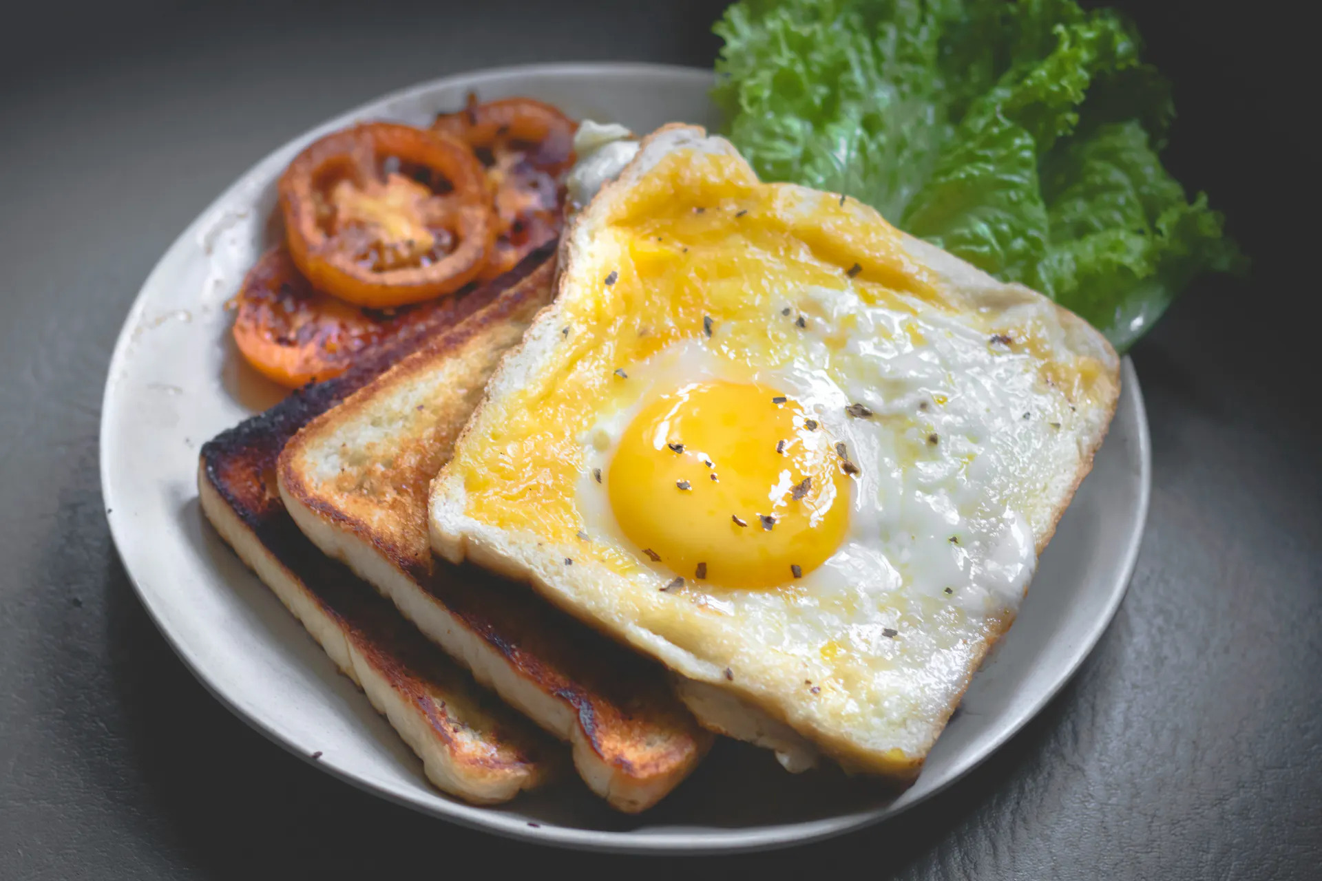 Toasted bread served with an egg on top on a white plate.
