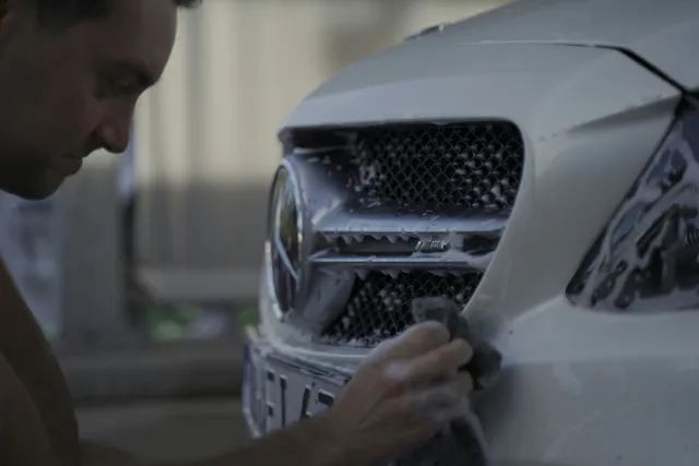 A close-up of someone washing and detailing the front of a vehicle.