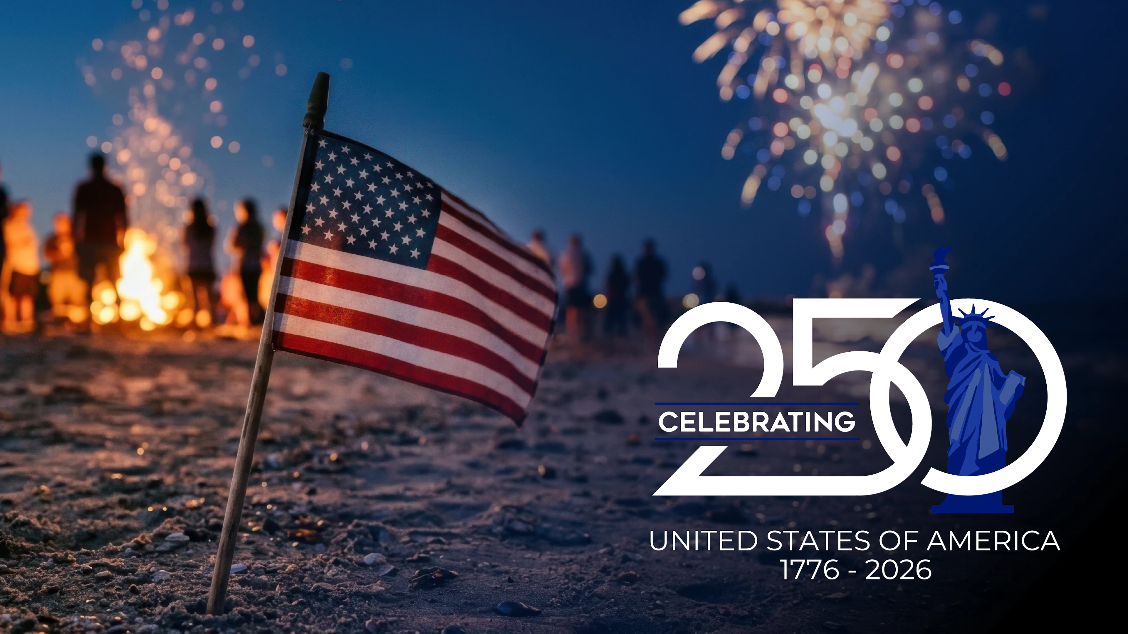 Handheld American flag stuck in the sand with a people, a bonfire and fireworks in the distance.
