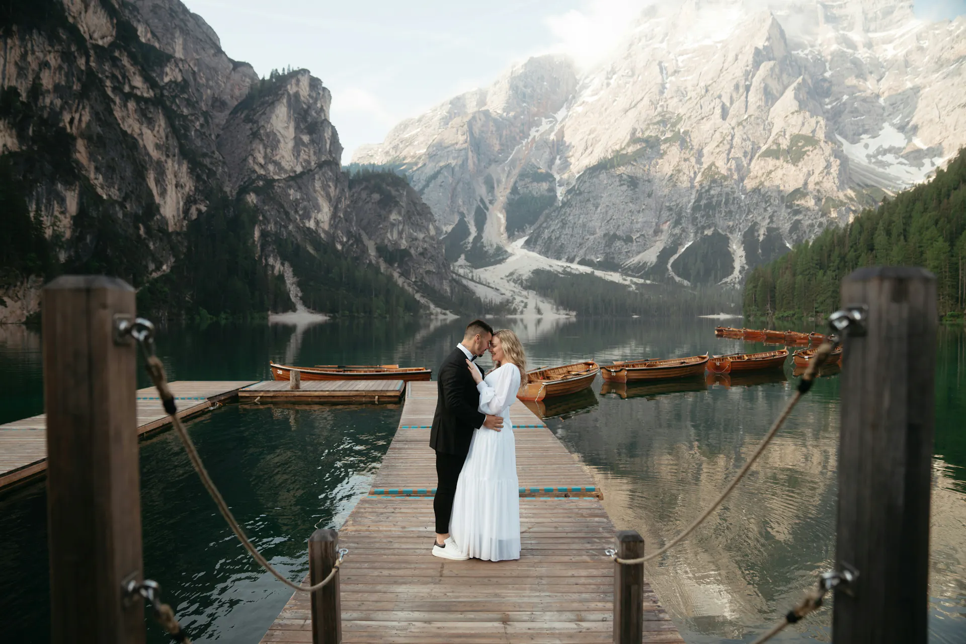 A bride and groom embracing on a bridge beneath mountains during their destination wedding at Lago di Braies in Northern Italy.