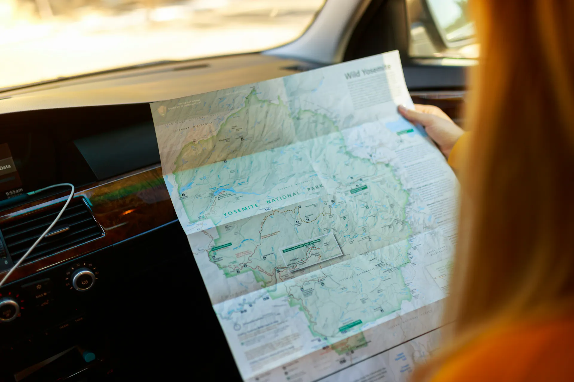 A woman holding a paper map inside of a van going down the road.