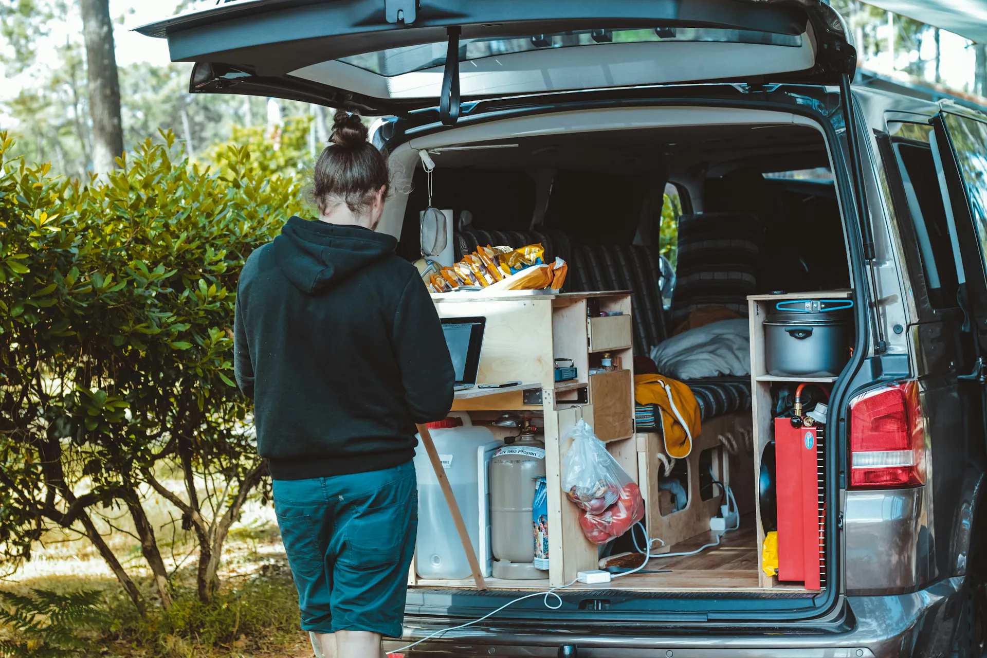 Someone standing at the rear of a travel van full of items.