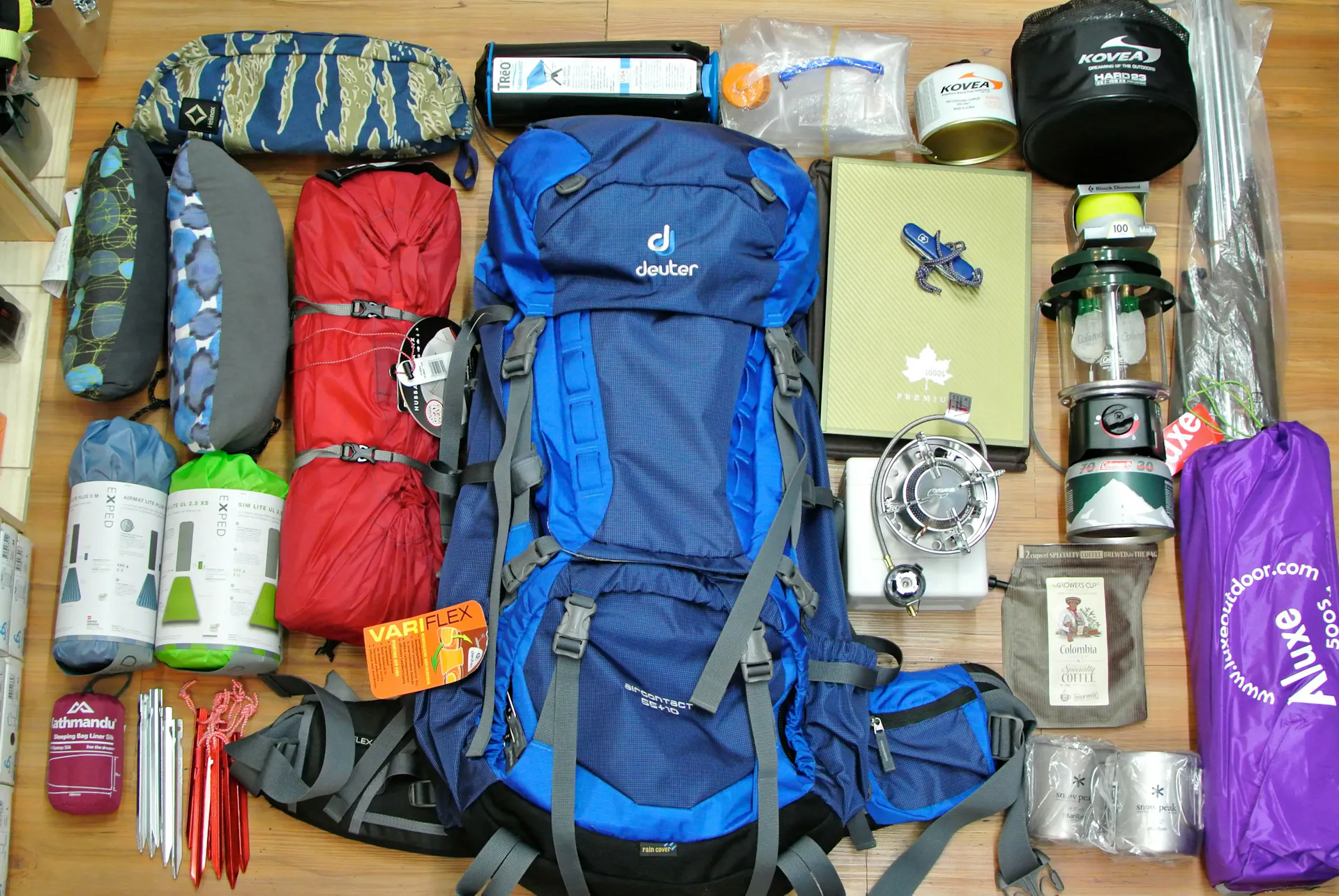 A selection of camping gear, such as a backpack, sleeping bag, lantern, portable fan, and more, laid out on a table.