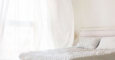 White bedroom with window open and air blowing through the window