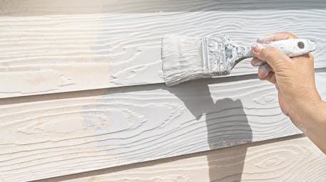Paint brush painting white paint on house siding 
