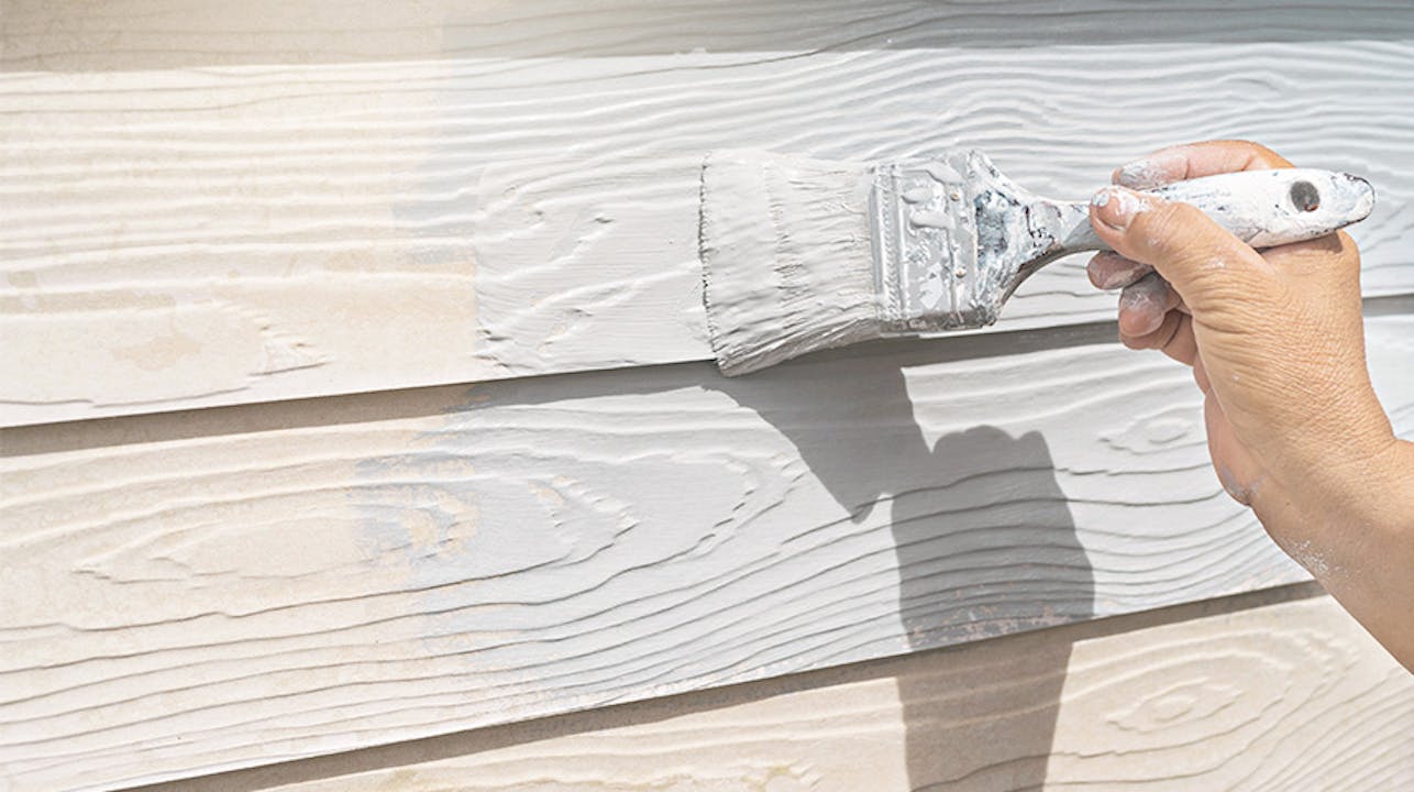 Paint brush painting white paint on house siding 