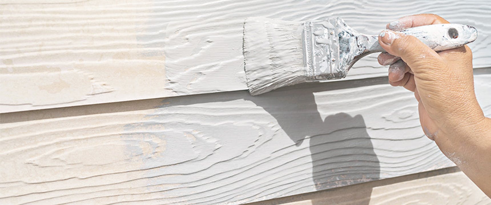 Paint brush painting white paint on house siding