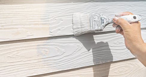 Paint brush painting white paint on house siding