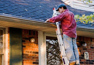 Man on ladder cleaning gutters