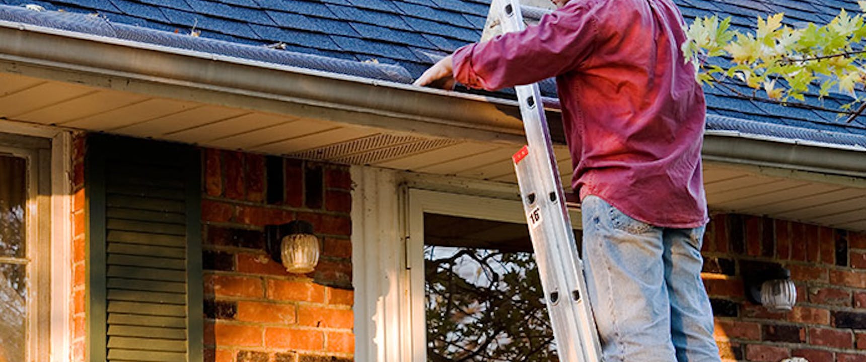Man on ladder cleaning gutters