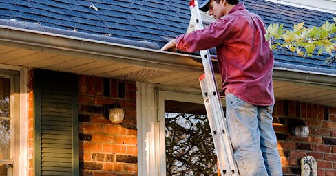 Man on ladder cleaning gutters