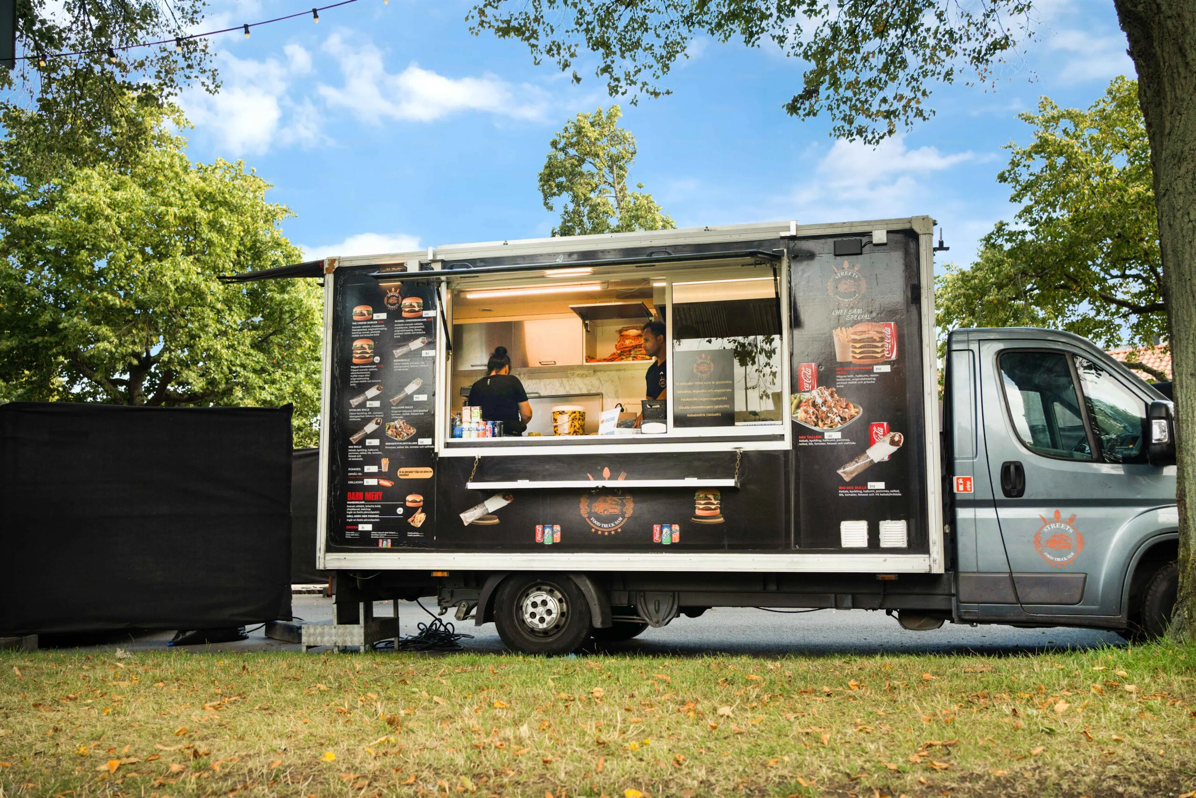 Streetfood Sams foodtruck uppställd i en park med personal som lagar mat