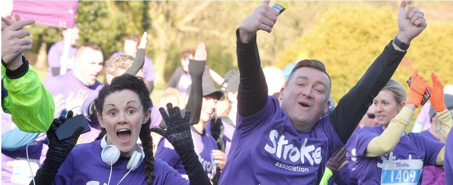 An excited man and woman cheering and throwing their hands in the air to celebrate completing a run, both dressed in purple t-shirts.