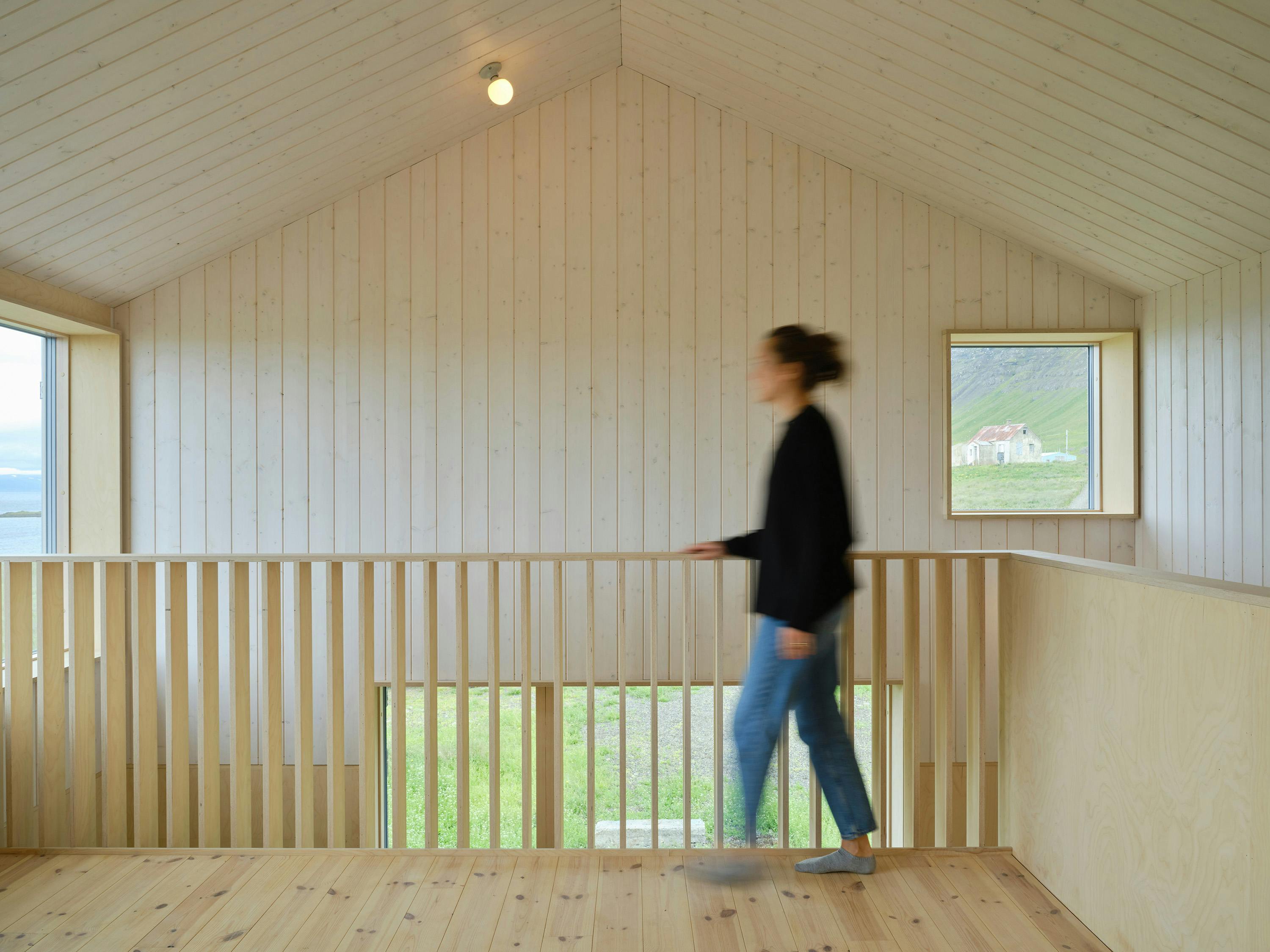 Woman walking in a modern and minimal scandinavian interior by architects Studio Bua. Glimpses of a green landscape are visible through picutre windows.