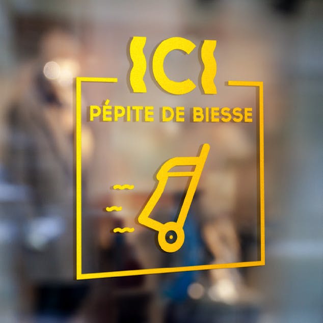 Sigle de certification et de recommandation issu de la nouvelle identité visuelle de la rue Biesse à Nantes, appliqué sur la vitrine d'un magasin.