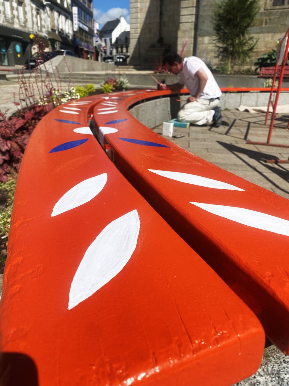 Signalétique urbaine réalisée sur la place d'une église, peinture d'un banc aux motifs de l'identité visuelle de la ville de Loudéac.