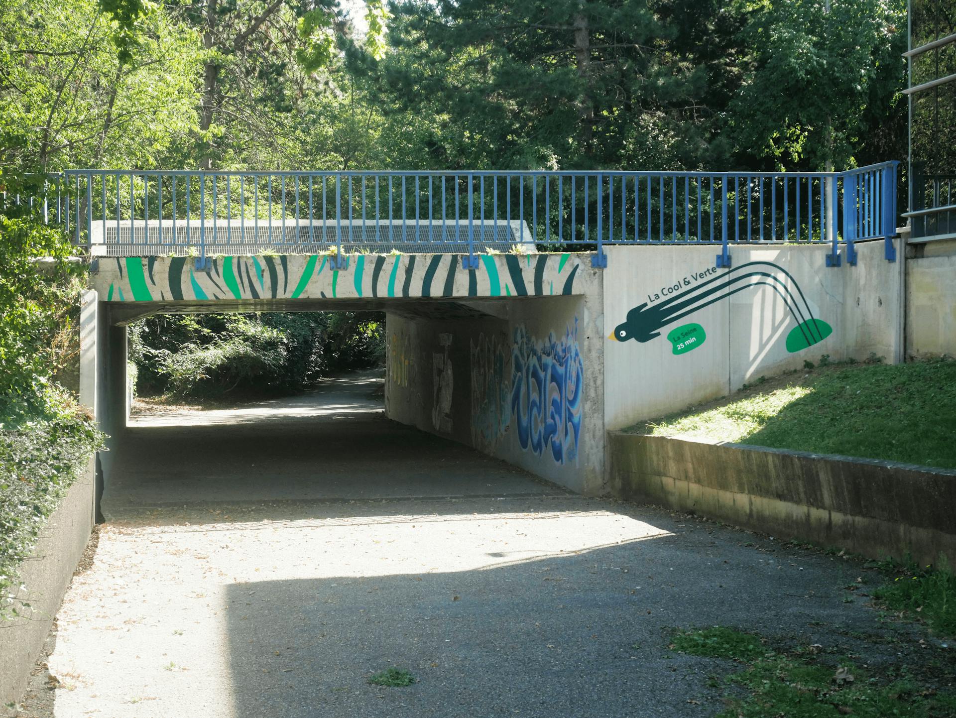 Le parcours de la Cool&Verte, représenté par des motifs peints sous un pont, menant vers la Seine. On aperçoit une signalétique indiquant que la Seine se trouve à 25 minutes à pieds de ce lieu.