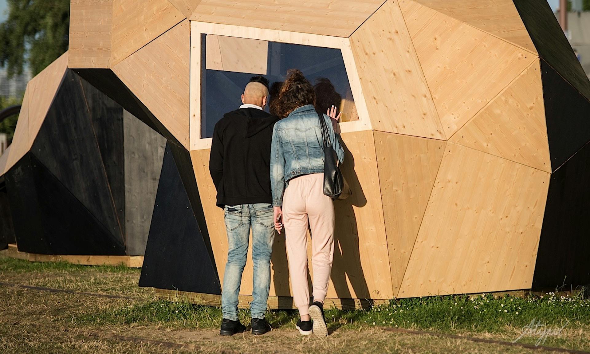 Deux personnes curieuses s'arrêtent pour admirer l'intérieur des modules en bois du concept "Pointe Noire" à l'Esperance café. 