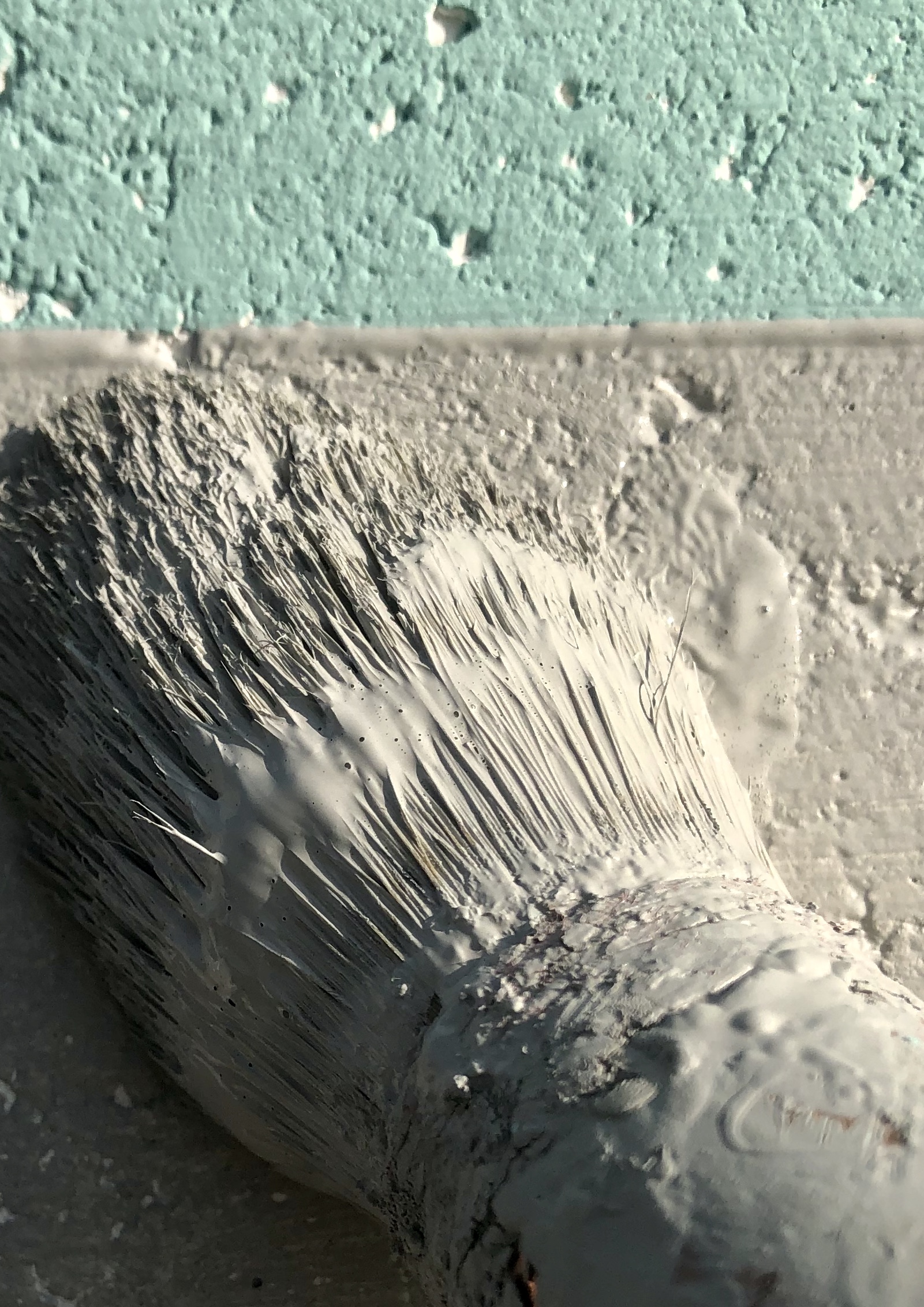 Plan rapproché d'un pinceau appliquant de la peinture grise sur un mur.