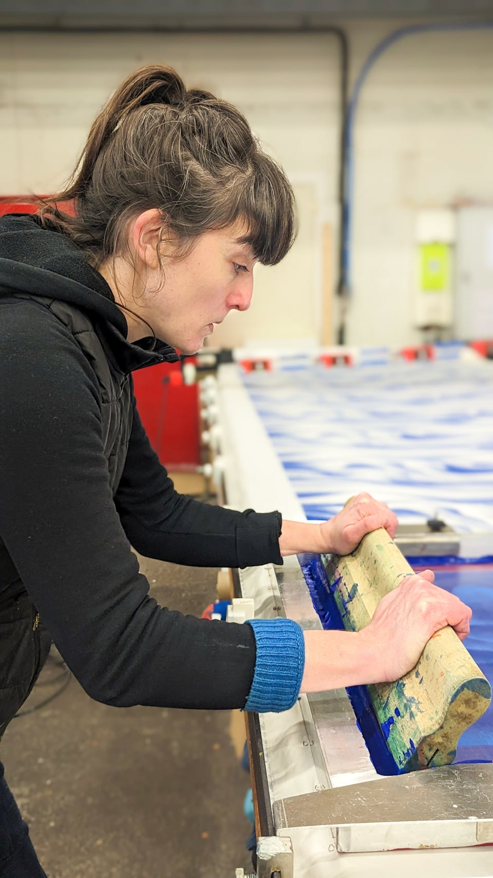 Clémence Regnier, ennoblisseur textile, poussant une raclette sur un cadre de sérigraphie pour une impression textile.