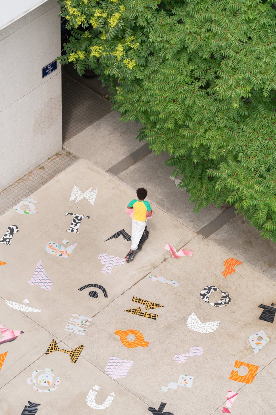 Un jeune homme roulant en trottinette électrique sur l'œuvre "le Champ des Signes" réalisée par l'agence de design graphique et street art Studio Katra.