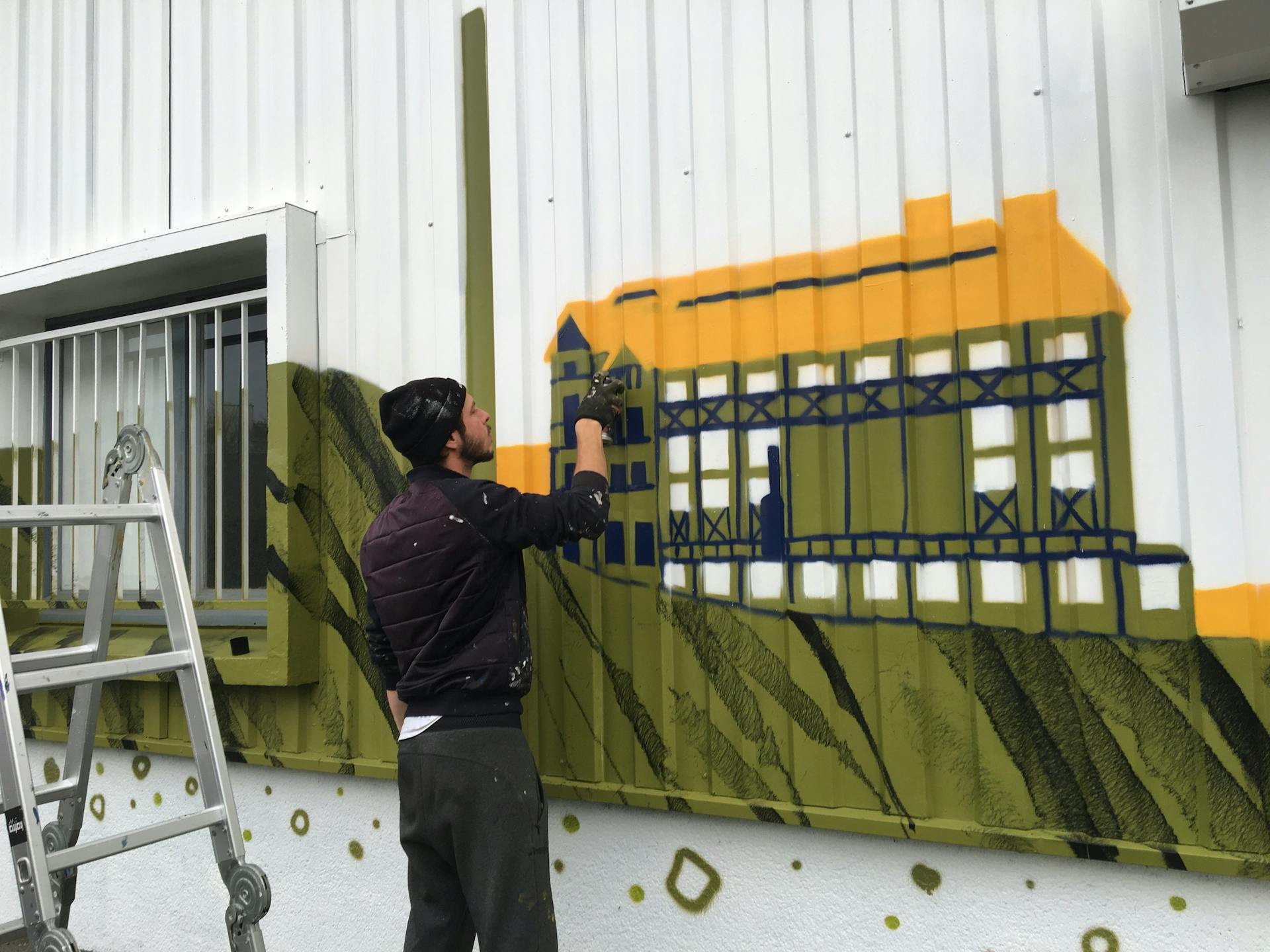 Camille Pansard, artiste peintre chez Studio Katra, effectue les finitions de la nouvelle fresque murale Labo Diva à l'aide d'une bombe de peinture.