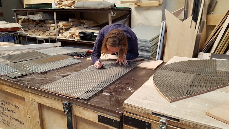 Jeune femme effectuant un tracé au crayon sur du bois pendant la création de la nouvelle enseigne du festival de la jeunesse nantaise.