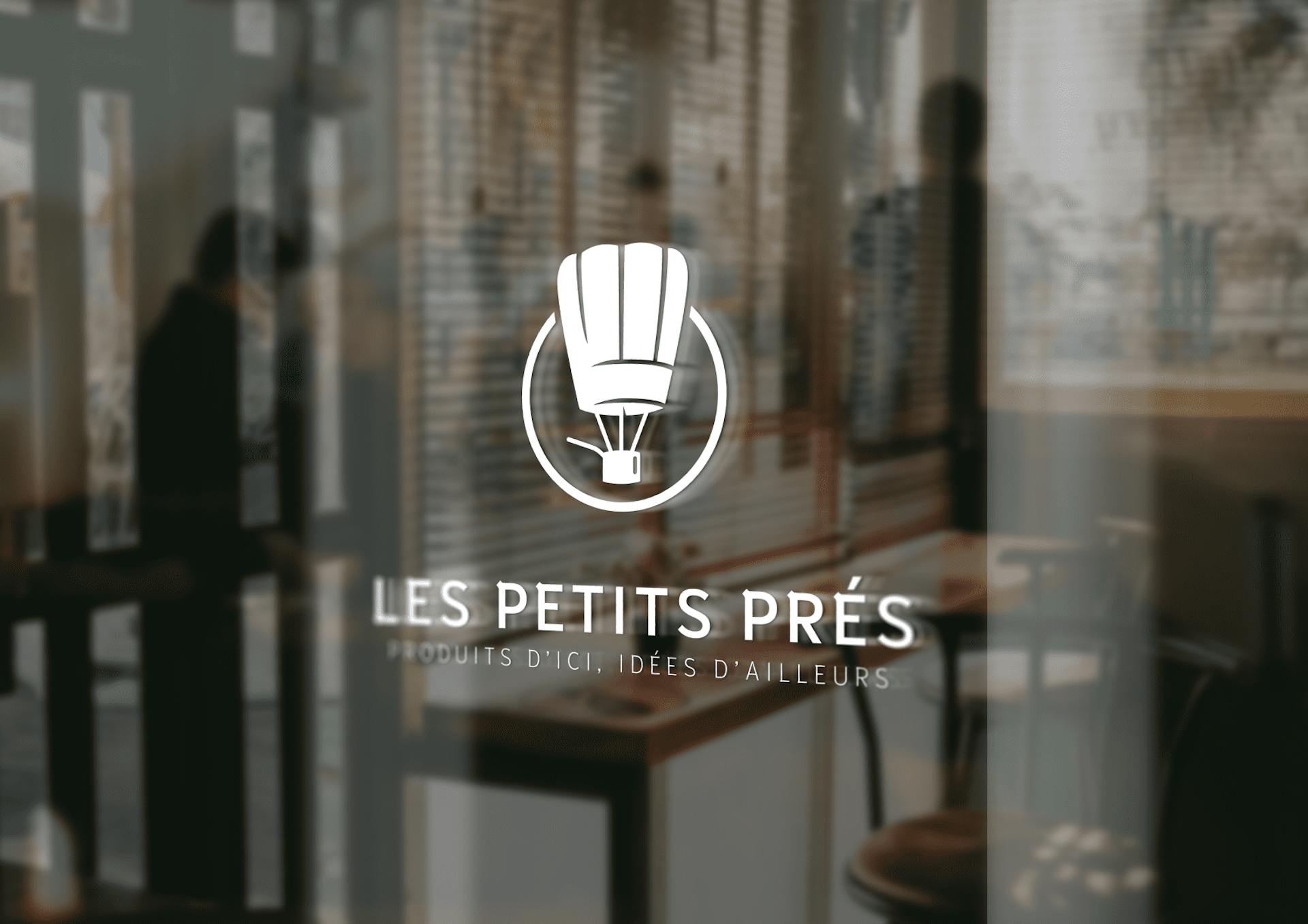 Mockup d'une vitrophanie du logo de l'enseigne "Les Petits Prés". Le logo représente une montgolfière en forme de casserole. 