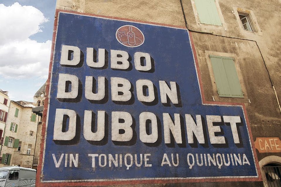 Peinture en lettres "Dubo, Dubon, Dubonnet" réalisée sur la façade d'un bâtiment.