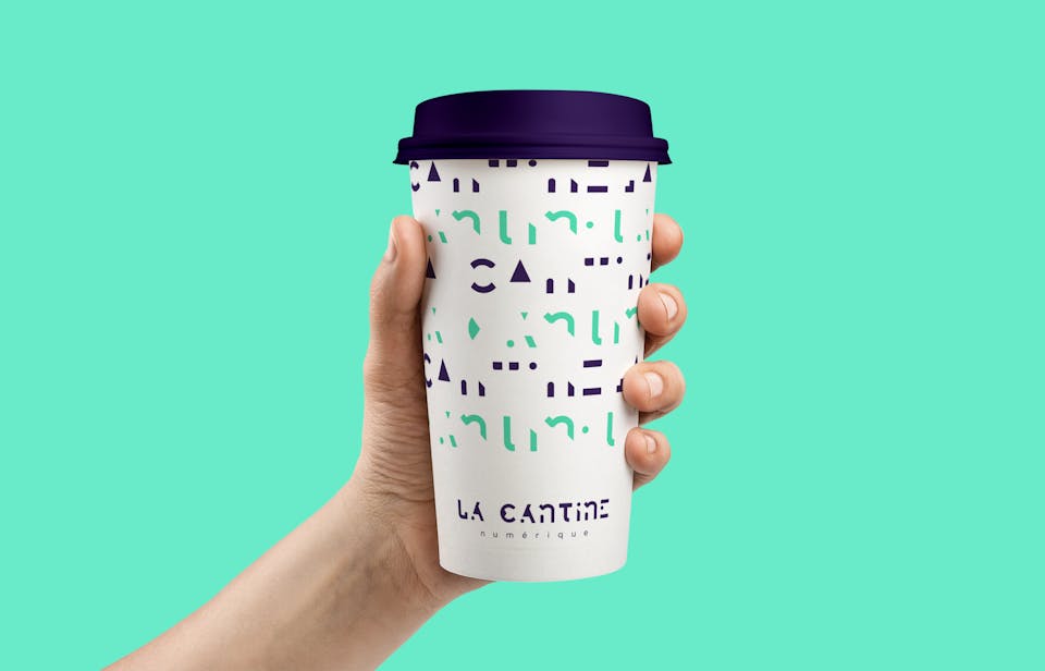 Un gobelet en carton portant la nouvelle identité de marque de la Cantine Numérique, imaginée par l'agence de design graphique Studio Katra.