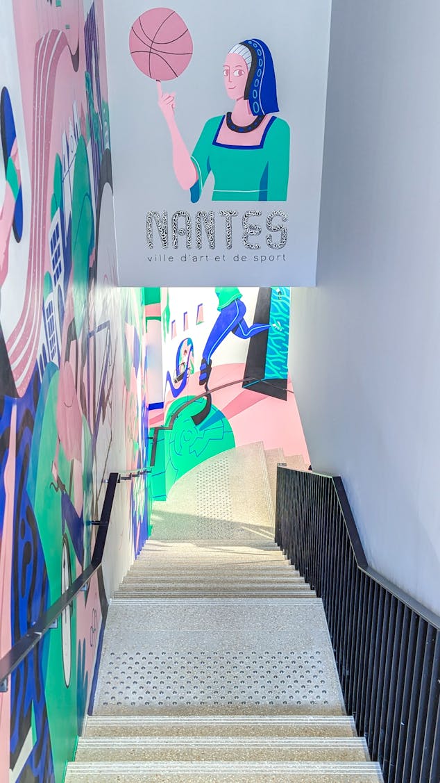 Une représentation d'Anne de Bretagne, réalisée par l'agence de Design Katra, faisant tourner un ballon de basket sur son doigt. En dessous est écrit : "Nantes, ville d'art et de sport".