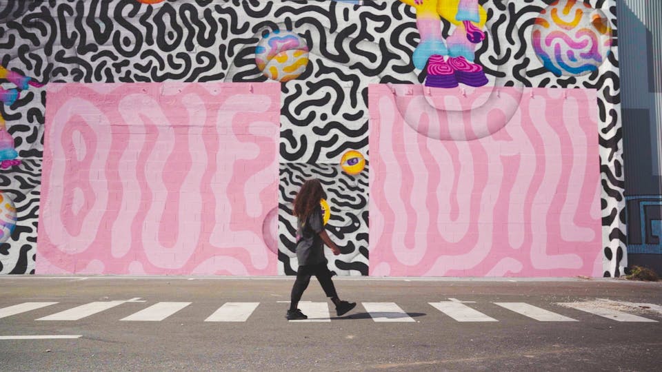 Ocü, Street artiste roumaine, passe devant un mur portant une énorme fresque murale qu'elle a réalisé.