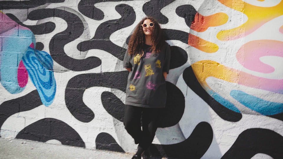 Ocü, Street artiste roumaine, est adossée sur un mur portant une énorme fresque murale qu'elle a réalisé.