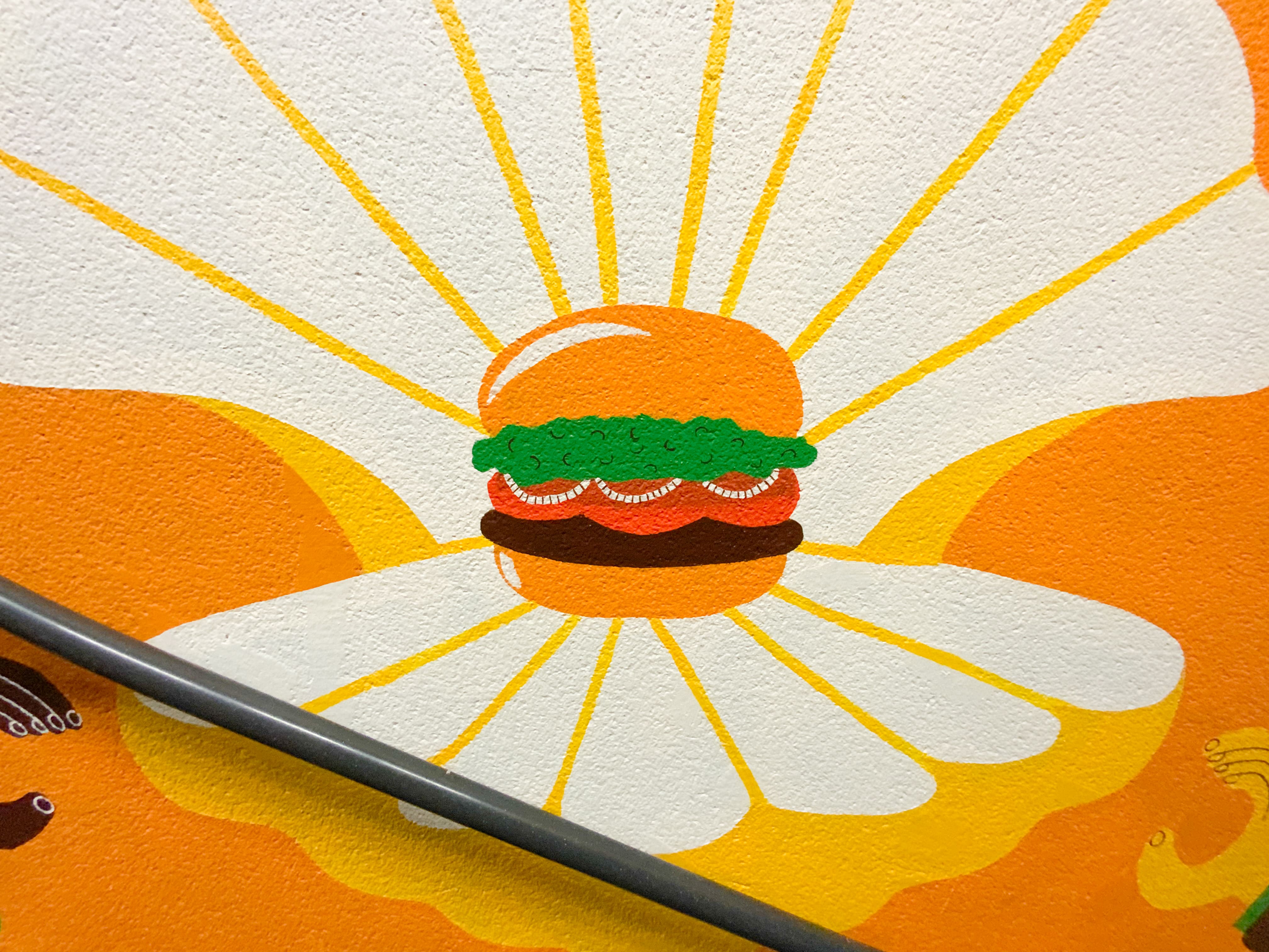 Une fresque murale extérieure réalisée au sein du Burger King de la Rochelle par l'agence de design graphique Studio Katra, représentant un burger rayonnant de lumière.
