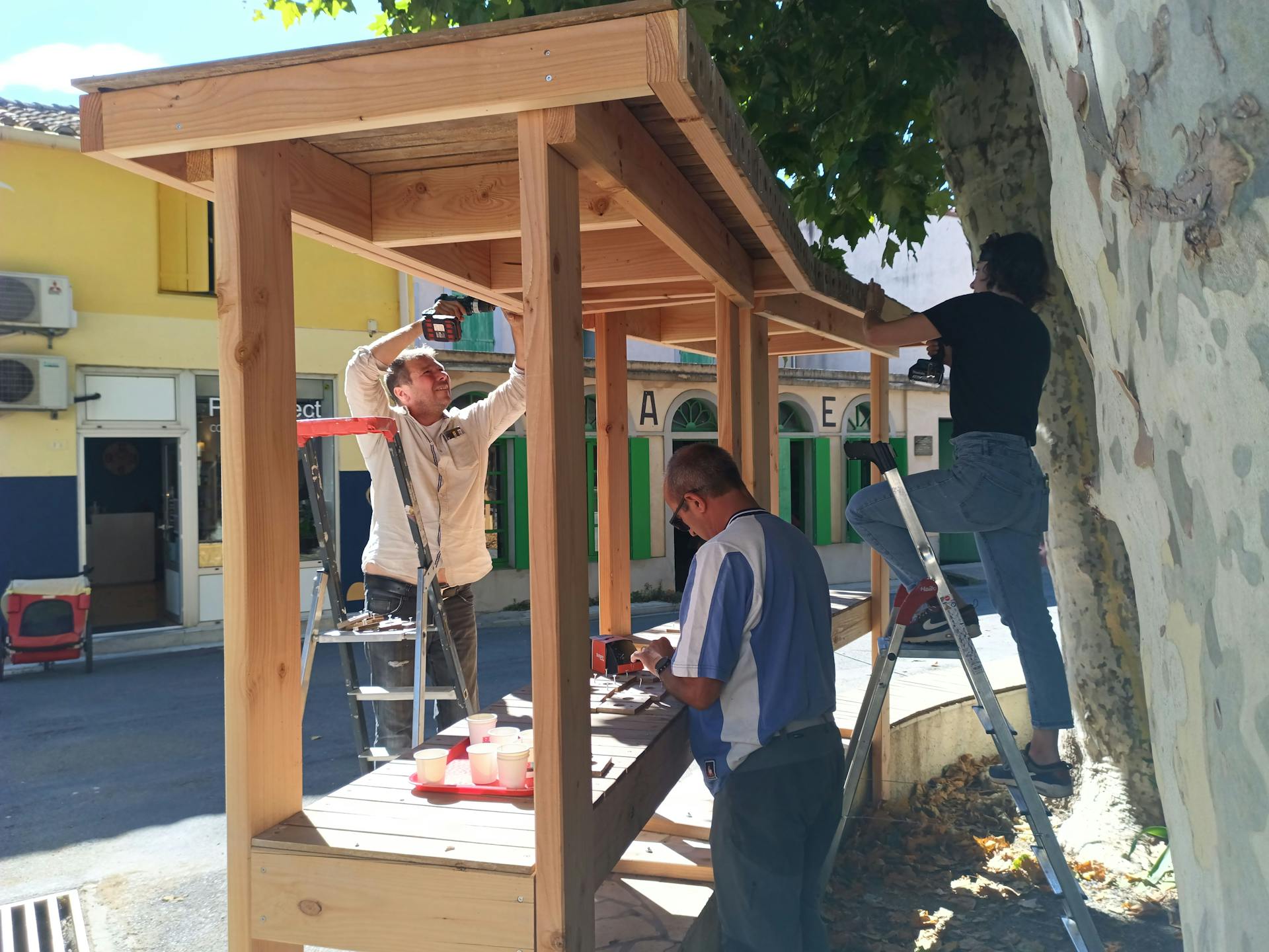 Les habitants bénévoles d'Argeliers travaillent à la construction d'une terrasse extérieure en bois réalisée sur la promenade Marcelin Albert de leur village en compagnie de l'agence de Design Studio Katra.
