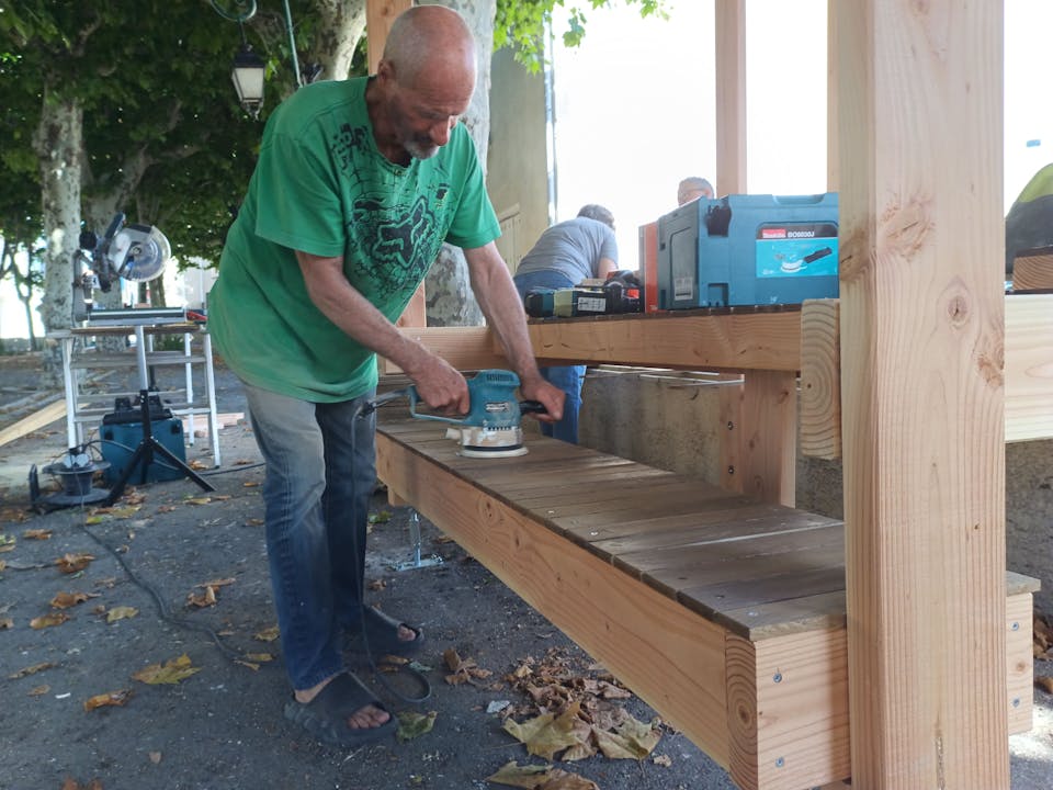 Les habitants bénévoles d'Argeliers travaillent à la construction d'une terrasse extérieure en bois réalisée sur la promenade Marcelin Albert de leur village en compagnie de l'agence de Design Studio Katra.