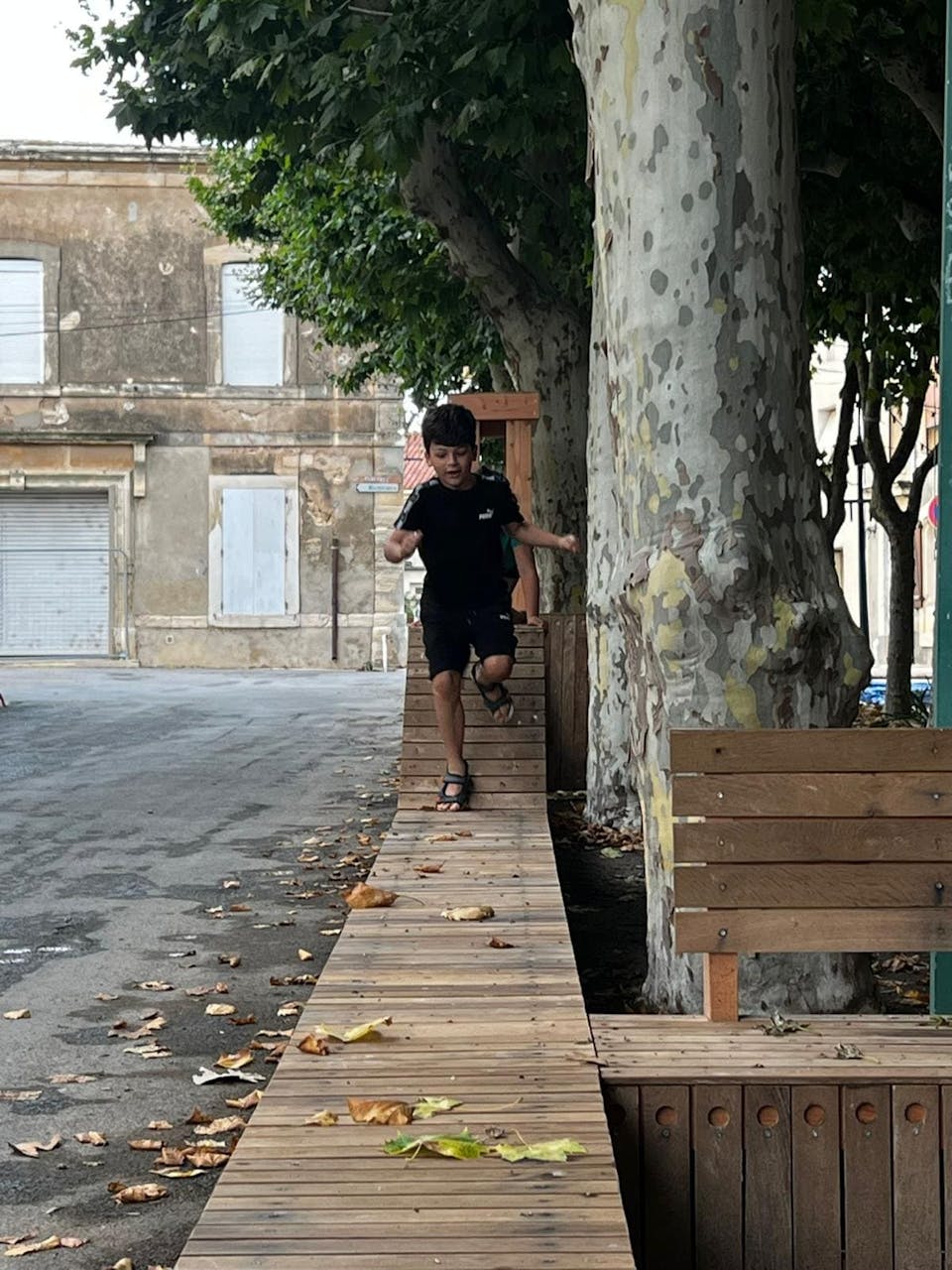 Un petit garçon court sur la nouvelle terrasse extérieure en bois réalisée sur la promenade Marcelin Albert du village d'Argeliers, par l'agence de design Studio Katra.