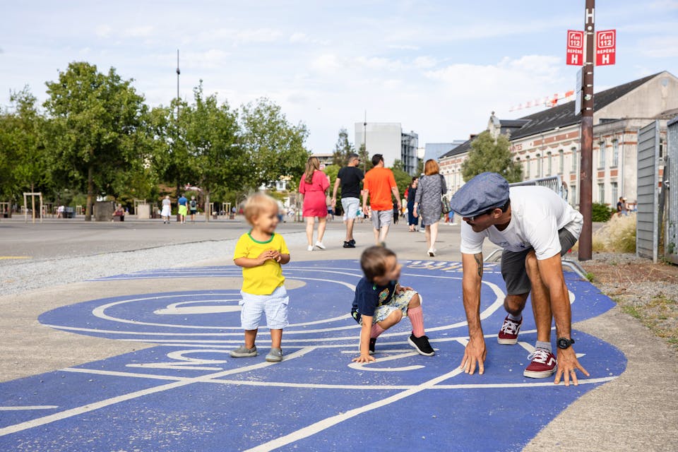 Des enfants s'apprêtent à faire la course avec leur père sur une piste d'athlétisme peinte au sol sur l'Île de Nantes.