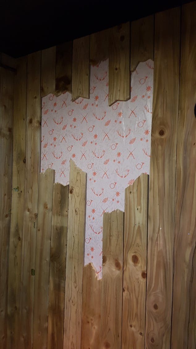 Effet de brèche créé dans le bois mural du photomaton, laissant visible des motifs à l'identité de Jägermeister.