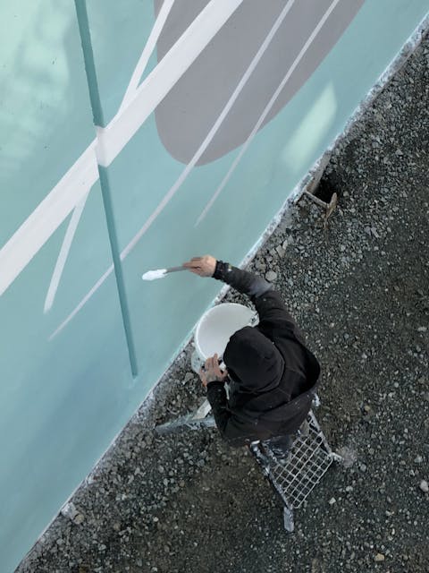 Plan en plongée d'un designer du Studio Katra appose une peinture murale extérieure sur la gare d'Angers Saint Laud.
