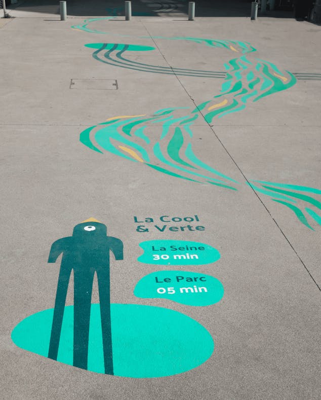 Une signalétique peinte au sol dans la Vallée d'Art du Déplacement, indiquant la proximité d'un parc et de la Seine au loin.