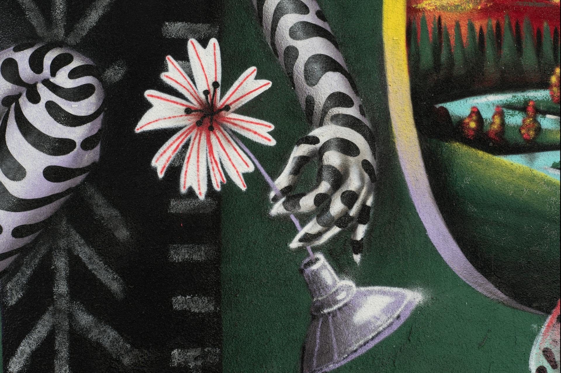 Sur cette partie de l'œuvre de street art des designer du Studio Katra, une main tient entre ses doigts une fleur.
