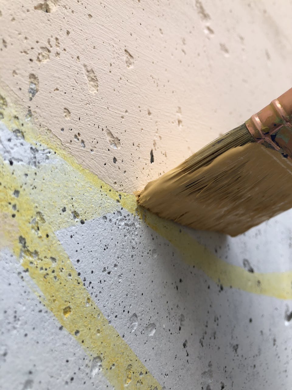 Un pinceau remplit une forme de couleur beige présente sur une fresque murale extérieure.