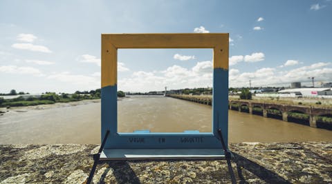 Un cadre de tableau posé sur le bord d'un pont, servant d'aperçu du paysage.