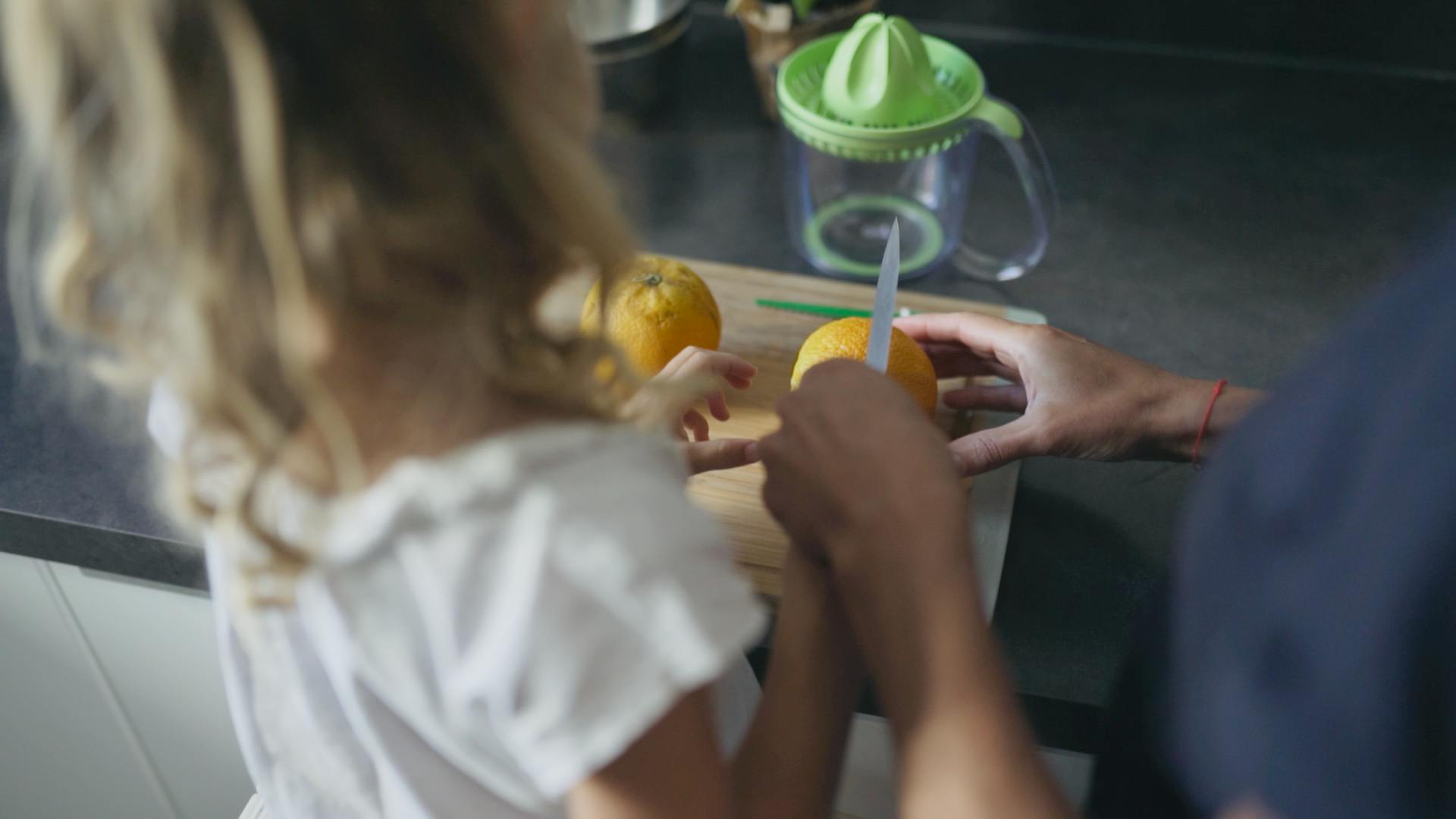 Une petite fille, aidée par sa mère, découpant une orange.