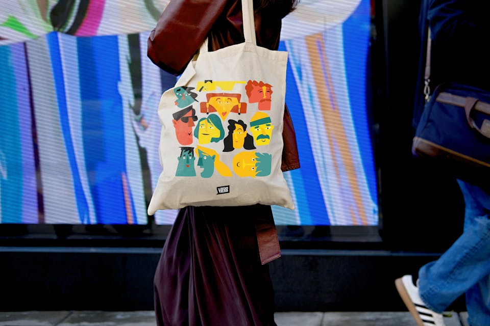 Mockup d'un tote bag basé sur la charte graphique du groupe V and B et son nouveau vocabulaire de formes. On y voit de multiples visages féminins et masculins géométriques.