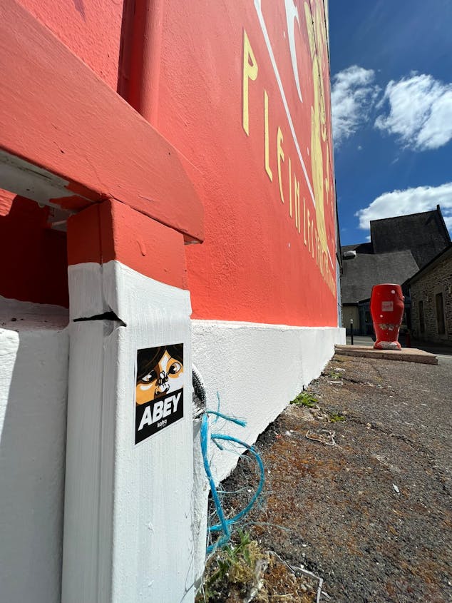 Un sticker "ABEY" posé sur le bas d'une fresque murale extérieure, dont le design est réalisé par le Studio Katra.