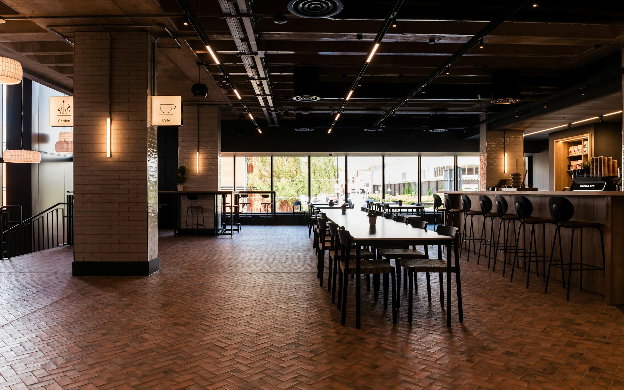 Wide shot of the cafe, showing a long table with chairs, bar seating, parquet floor and tiled pillars.