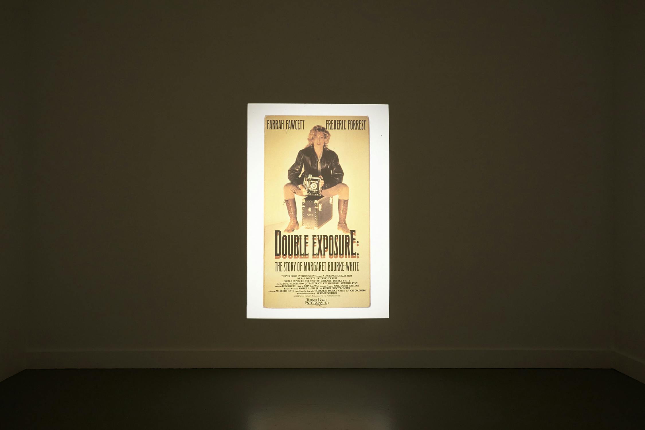 A poster for the movie "Double Exposure" is illuminated on a blank wall. The poster features a person sitting in a director's chair, holding a camera, with the movie title and credits written below. The background of the room is dark, highlighting the poster.
